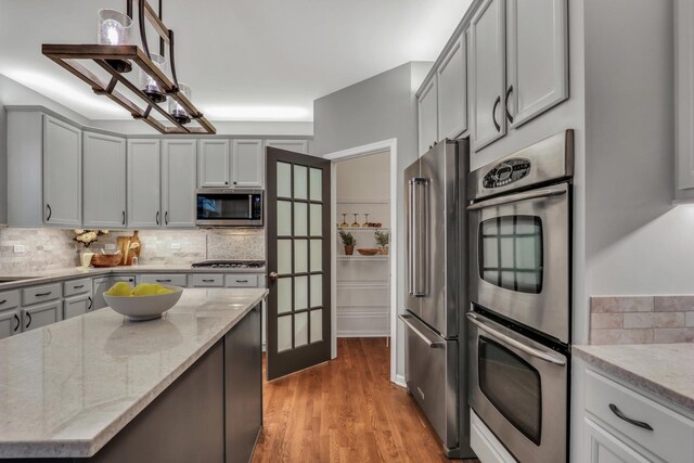 kitchen featuring stainless steel appliances, light wood-style floors, decorative backsplash, light stone counters, and gray cabinets