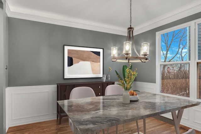 dining room featuring a wainscoted wall, wood finished floors, ornamental molding, a decorative wall, and a notable chandelier