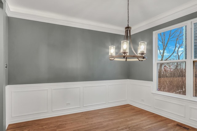 spare room with a wainscoted wall, an inviting chandelier, wood finished floors, visible vents, and crown molding