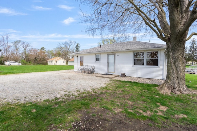 back of house featuring a shingled roof, a chimney, and a yard