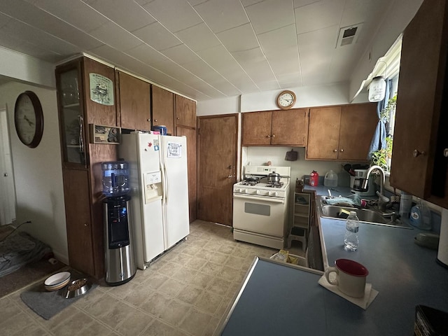 kitchen with a sink, brown cabinetry, white appliances, light floors, and visible vents