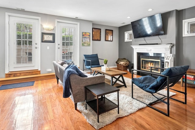 living area with wood finished floors, a glass covered fireplace, and recessed lighting