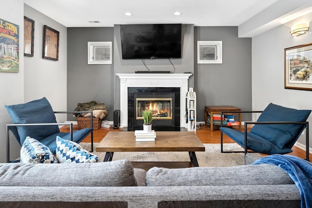 living room featuring wood finished floors, a glass covered fireplace, recessed lighting, and baseboards