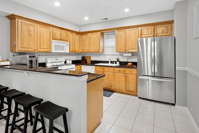 kitchen featuring white appliances, a sink, a peninsula, light tile patterned floors, and dark stone counters