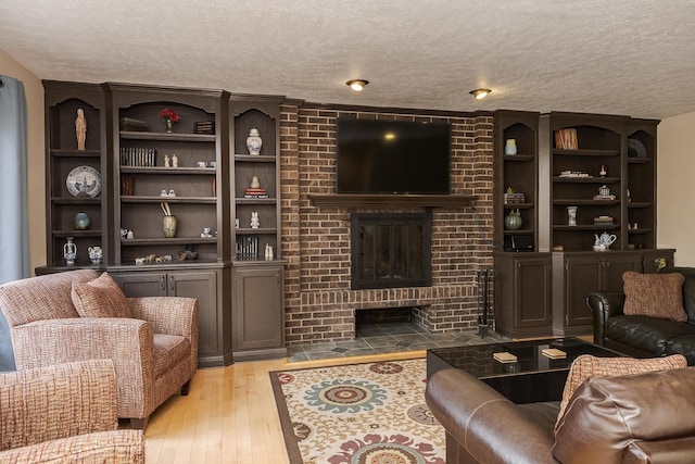 living room featuring light wood-style flooring, a brick fireplace, and a textured ceiling
