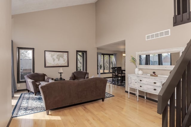 living room with light wood-style floors, visible vents, baseboards, and a high ceiling