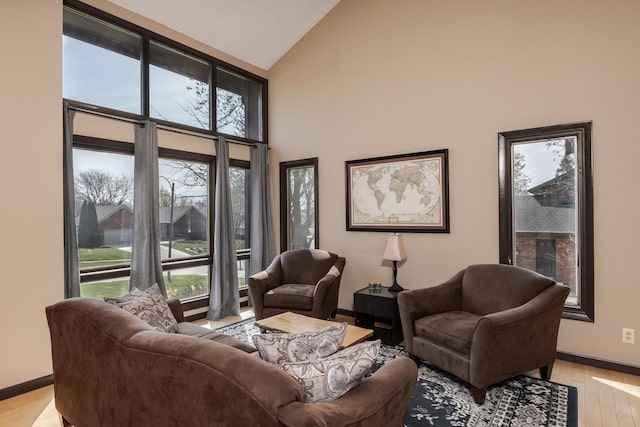 living room with high vaulted ceiling, baseboards, and light wood-style flooring