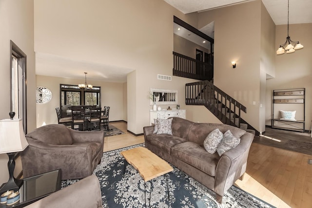 living room with stairway, hardwood / wood-style flooring, an inviting chandelier, a high ceiling, and visible vents