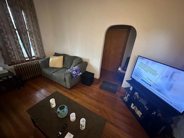 living room with radiator heating unit, wood finished floors, and arched walkways