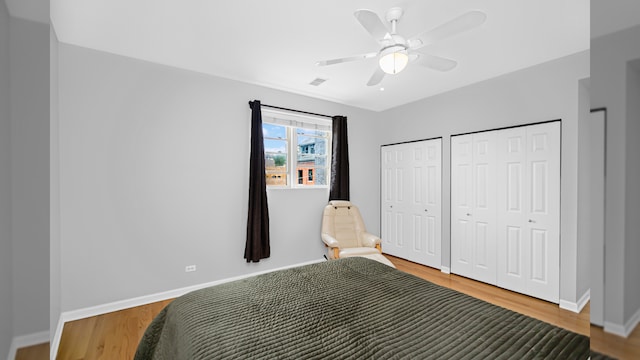 bedroom featuring two closets, wood finished floors, baseboards, and a ceiling fan