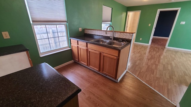 kitchen with baseboards, dark countertops, a sink, and light wood-type flooring