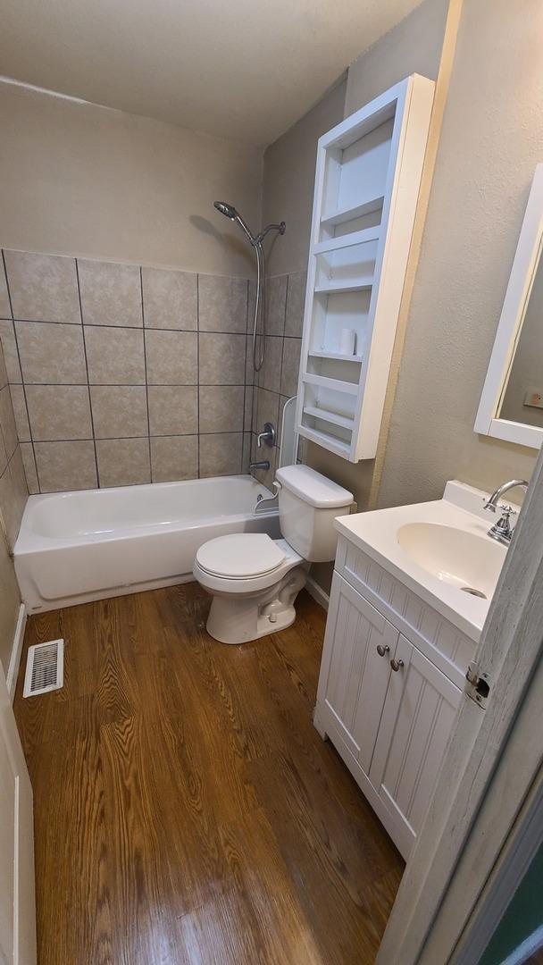 bathroom featuring wood finished floors, vanity, tub / shower combination, toilet, and visible vents