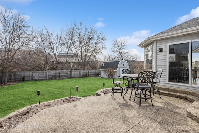 view of patio with a storage unit, outdoor dining space, an outbuilding, and a fenced backyard