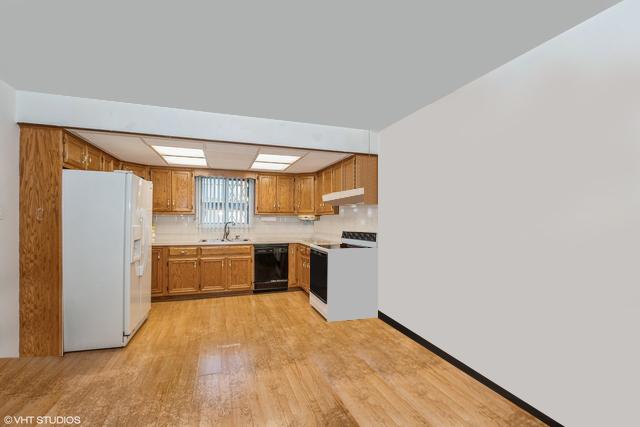 kitchen with light wood finished floors, a sink, white appliances, brown cabinets, and under cabinet range hood