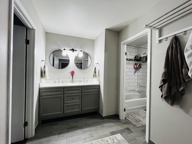 bathroom with shower / bath combination, wood finished floors, a sink, and double vanity