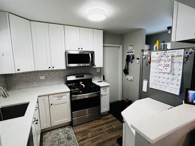 kitchen with white cabinets, dark wood-style floors, a sink, backsplash, and appliances with stainless steel finishes