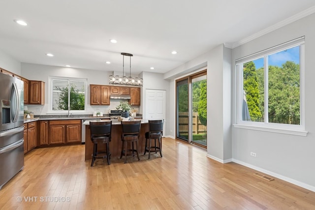 1635 Arlington Ln, Gurnee, IL 60031 - kitchen featuring appliances with stainless steel finishes, under cabinet range hood, brown cabinets, a breakfast bar, and light wood-style flooring