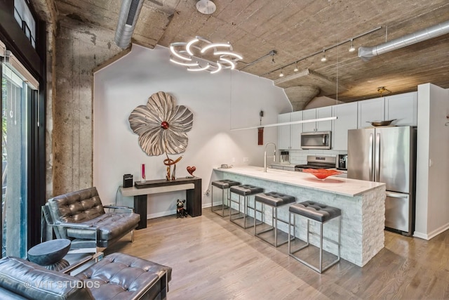 kitchen with stainless steel appliances, a sink, light countertops, a breakfast bar, and rail lighting