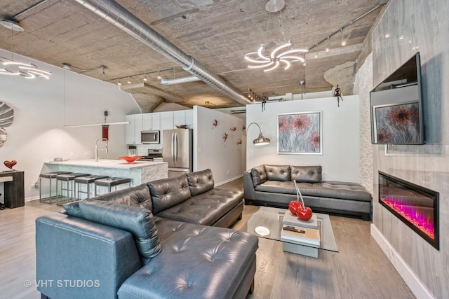 living area with a glass covered fireplace, light wood-style flooring, and baseboards