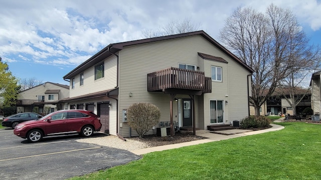 back of house with a lawn, uncovered parking, and a balcony