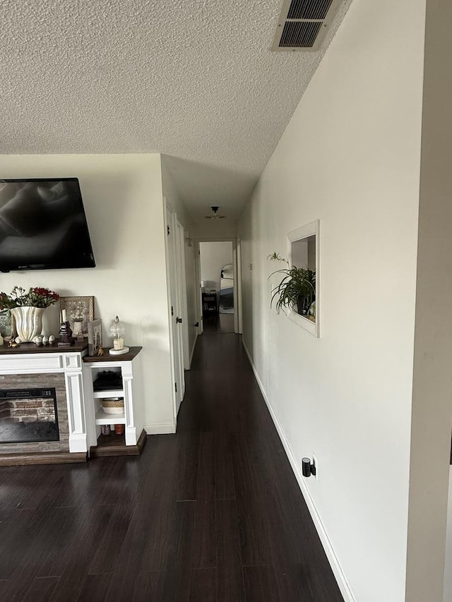 hallway featuring a textured ceiling, baseboards, wood finished floors, and visible vents