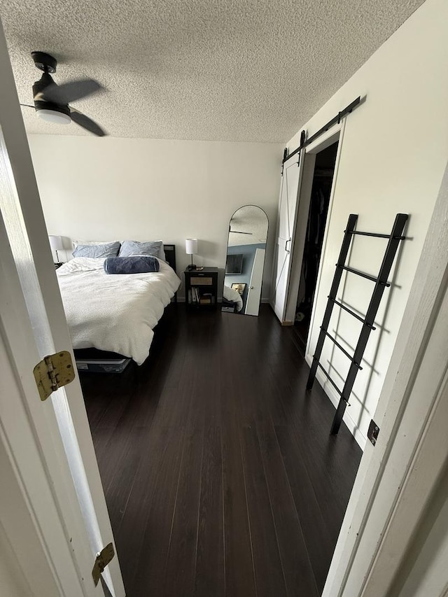 bedroom with a textured ceiling, dark wood-style floors, and a barn door