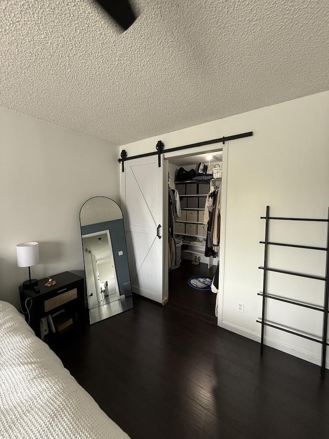 bedroom with a textured ceiling, dark wood-style floors, a barn door, and a spacious closet