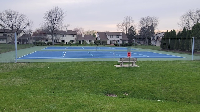 view of tennis court featuring a yard, fence, community basketball court, and a residential view
