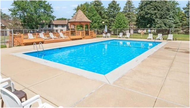 community pool with a gazebo, fence, a wooden deck, and a patio area