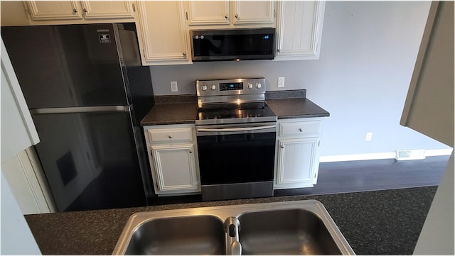 kitchen with a sink, freestanding refrigerator, stainless steel electric range oven, white cabinets, and dark countertops