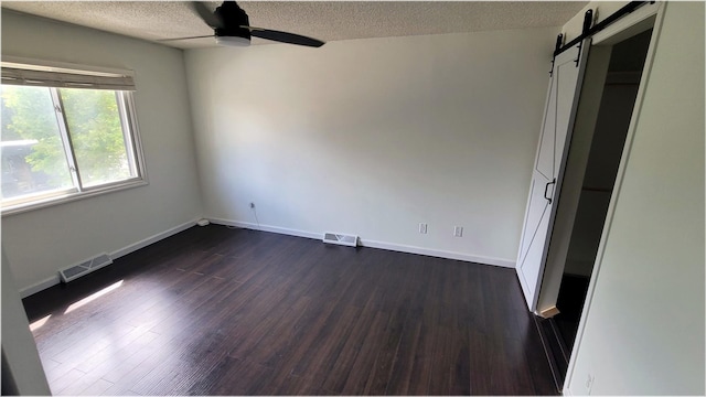 interior space featuring a textured ceiling, a barn door, dark wood-type flooring, and visible vents