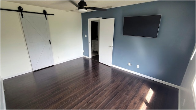 unfurnished bedroom with visible vents, a barn door, baseboards, ceiling fan, and dark wood-style floors