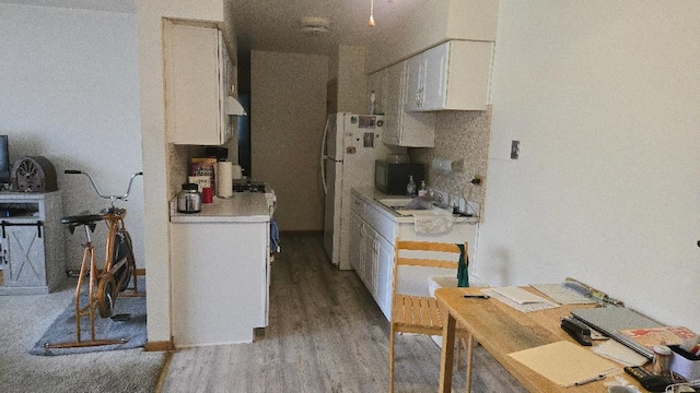 kitchen with light countertops, wood finished floors, a sink, freestanding refrigerator, and white cabinetry