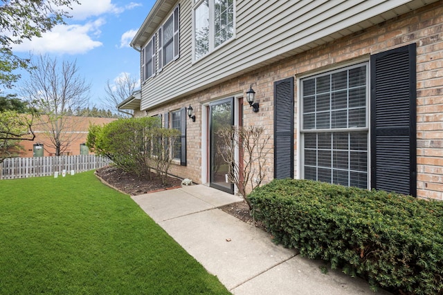 entrance to property featuring brick siding, fence, and a yard