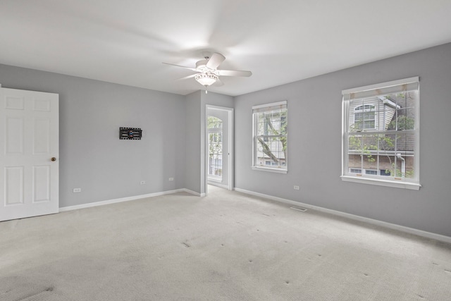 carpeted spare room featuring a healthy amount of sunlight, a ceiling fan, and baseboards