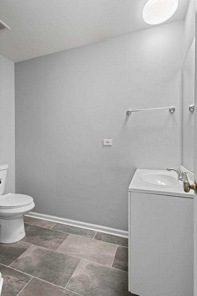 half bath with toilet, vanity, baseboards, stone finish floor, and visible vents