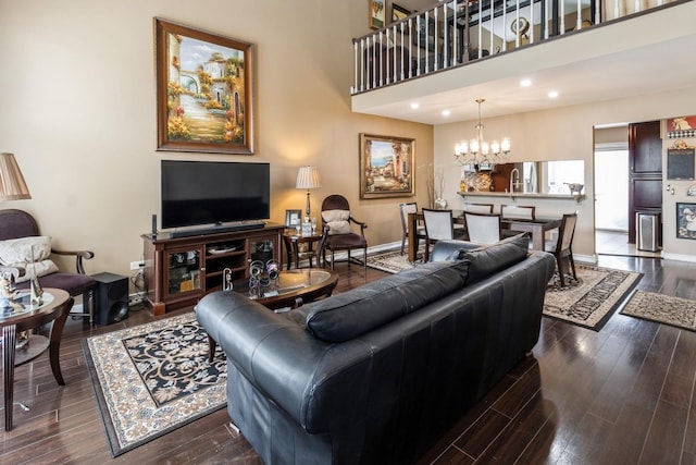 living room featuring recessed lighting, a high ceiling, dark wood-style floors, an inviting chandelier, and baseboards