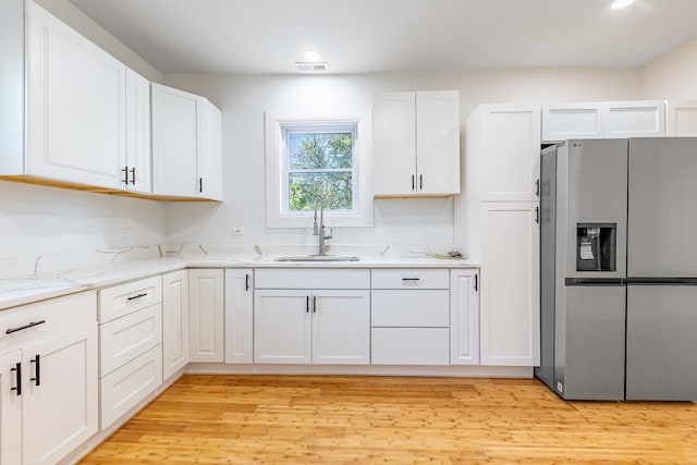 kitchen featuring a sink, light wood-style flooring, white cabinets, stainless steel refrigerator with ice dispenser, and light stone countertops
