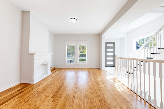 unfurnished living room featuring light wood-style flooring, baseboards, and a fireplace with raised hearth