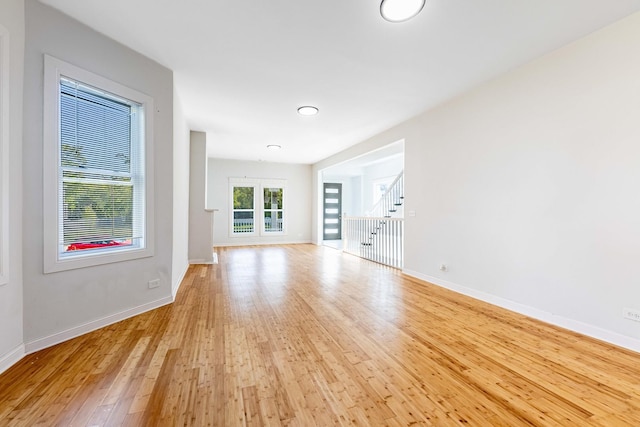unfurnished living room featuring stairs, baseboards, and light wood-style floors