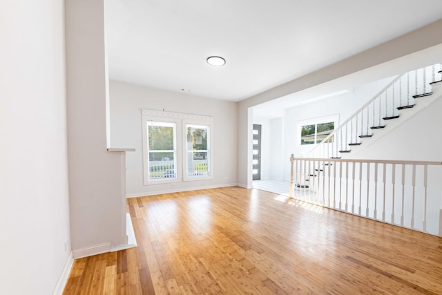 unfurnished living room featuring baseboards, stairs, and hardwood / wood-style flooring