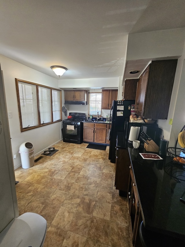 kitchen featuring under cabinet range hood, dark countertops, stone finish flooring, and black appliances