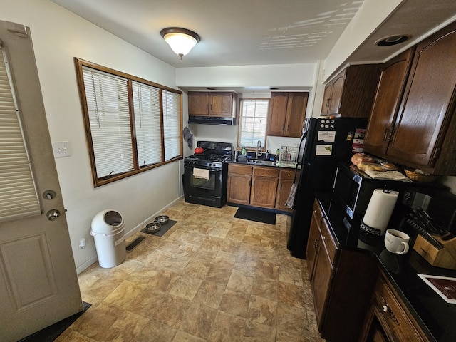 kitchen featuring stone finish flooring, a sink, baseboards, black appliances, and under cabinet range hood