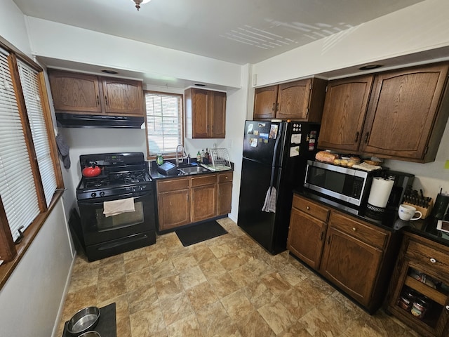 kitchen featuring dark countertops, a sink, stone finish flooring, under cabinet range hood, and black appliances