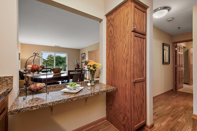 10300 Village Circle Dr Unit 1109, Palos Park, IL 60464 - kitchen with dark stone counters, baseboards, a kitchen bar, wood finished floors, and brown cabinets
