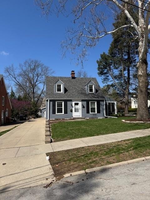 cape cod home with a chimney, driveway, and a front yard