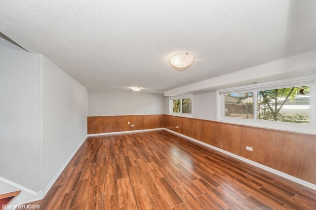unfurnished room with wood finished floors, a textured ceiling, wainscoting, baseboards, and wooden walls