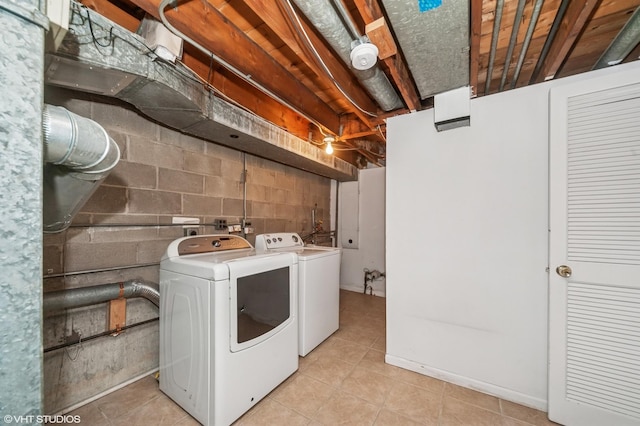 clothes washing area with washer and dryer, light tile patterned flooring, and concrete block wall