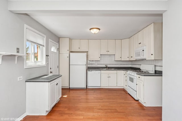 kitchen with white appliances, dark countertops, decorative backsplash, light wood finished floors, and a sink