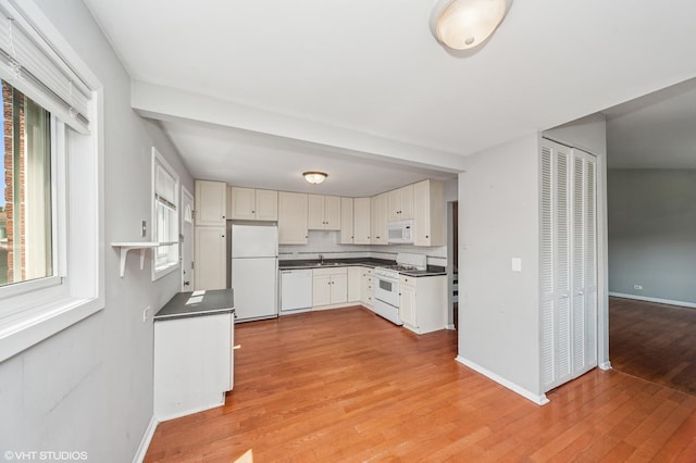 kitchen with white appliances, dark countertops, a sink, light wood-style flooring, and baseboards
